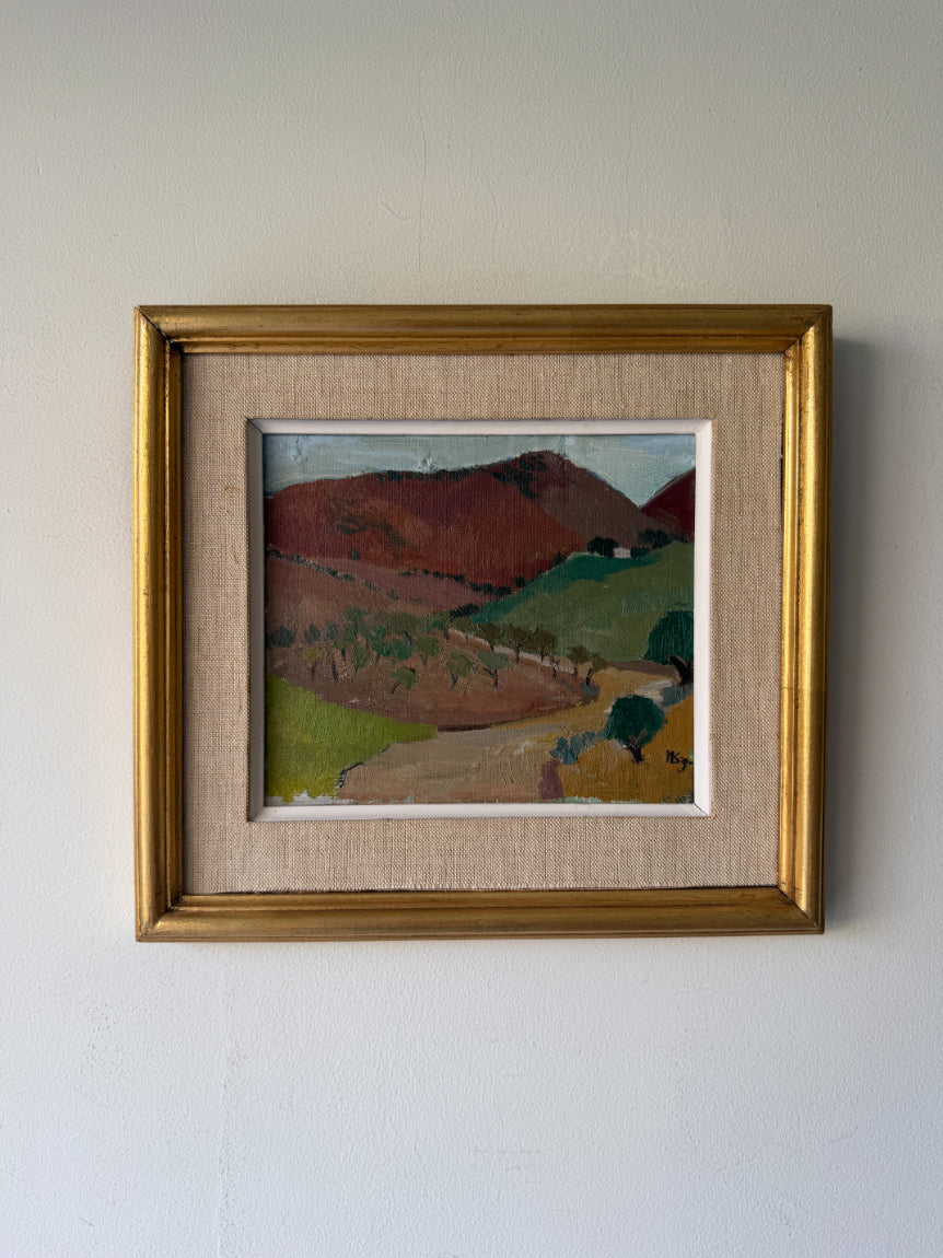 A framed vintage landscape oil painting of rolling hills and vineyards, featuring a rustic gold frame and a textured beige mat board. Available at Hue. 
