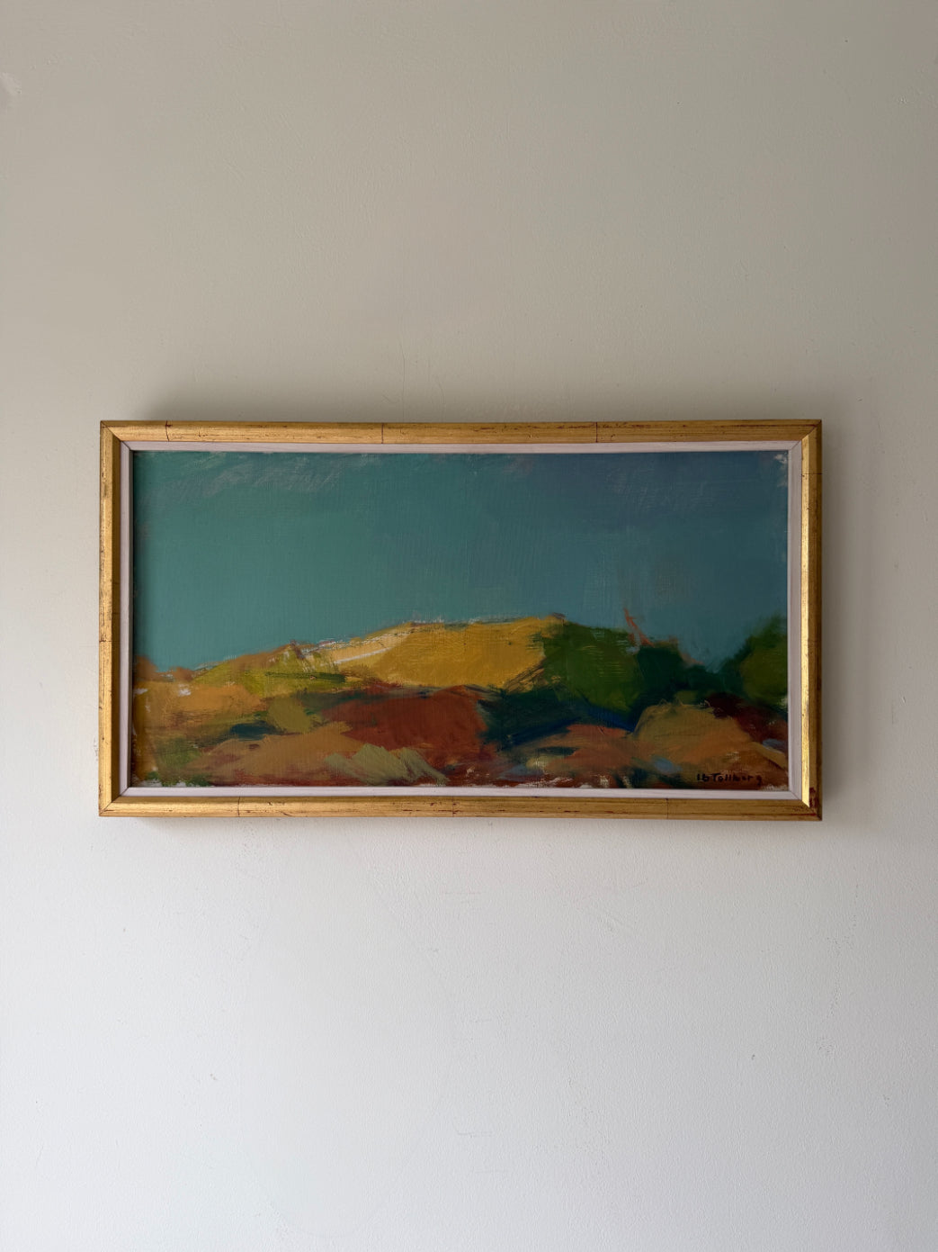 A framed vintage landscape painting. The artwork depicts rolling hills in earthy tones of green, yellow, brown, and red under a deep teal-blue sky, enclosed in a thin vintage gold frame. Available at Hue. 