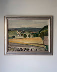 A framed vintage landscape oil painting featuring green hills, trees, and a golden field, housed in a distressed silver frame. Available at Hue. 
