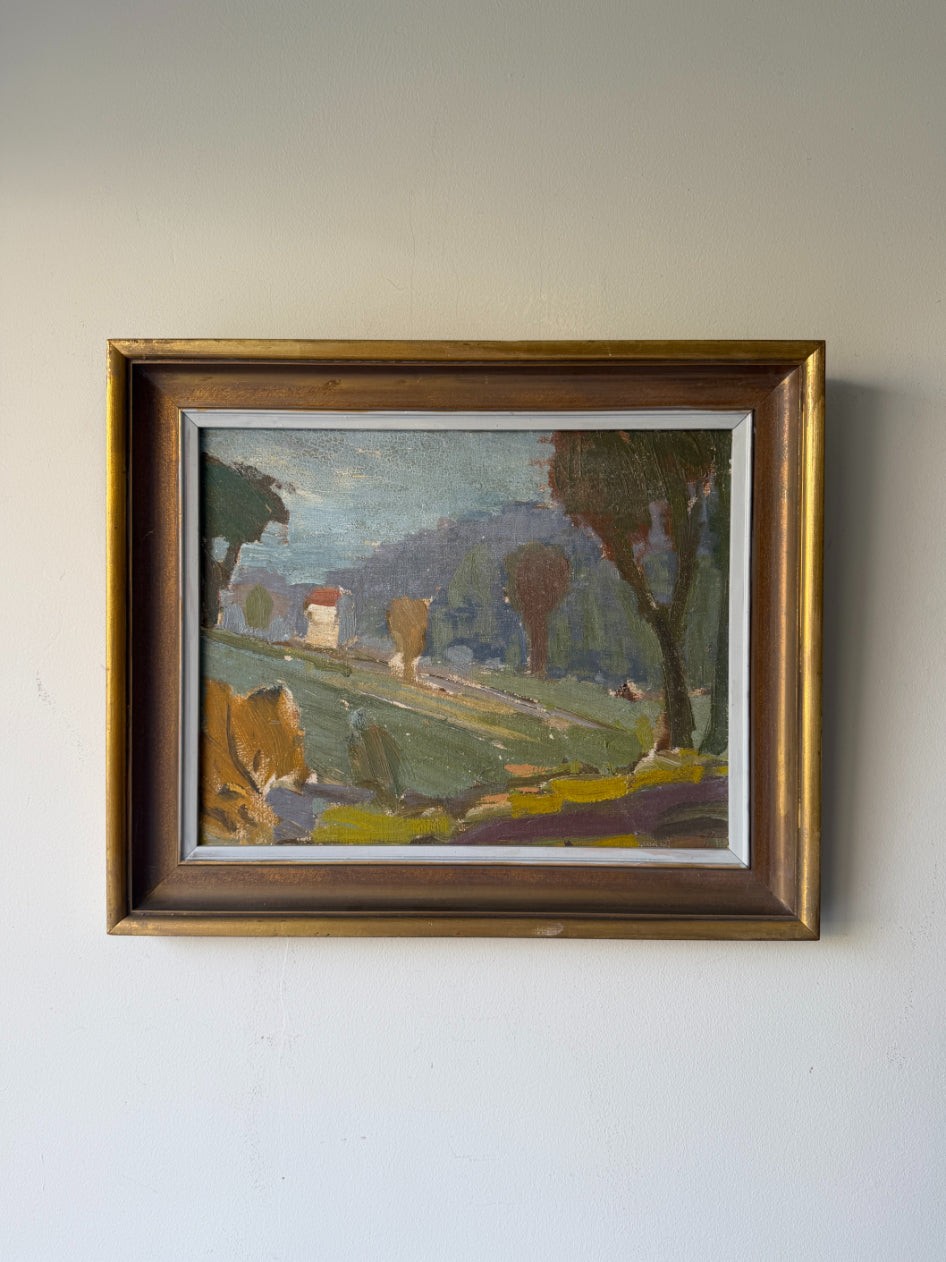 A framed vintage landscape oil painting  depicting a rural Italian-style scene with green fields, trees, hills, and a small house, enclosed in a rustic gold-toned wooden frame. Available at Hue. 