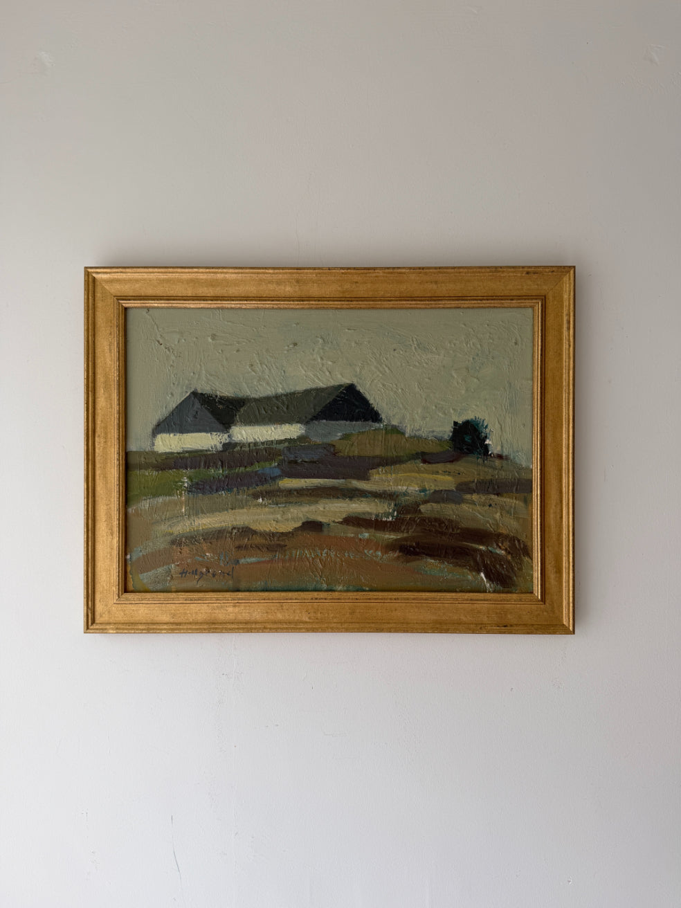 A framed vintage landscape painting featuring a house and field, housed in a gold frame. Available at Hue. 