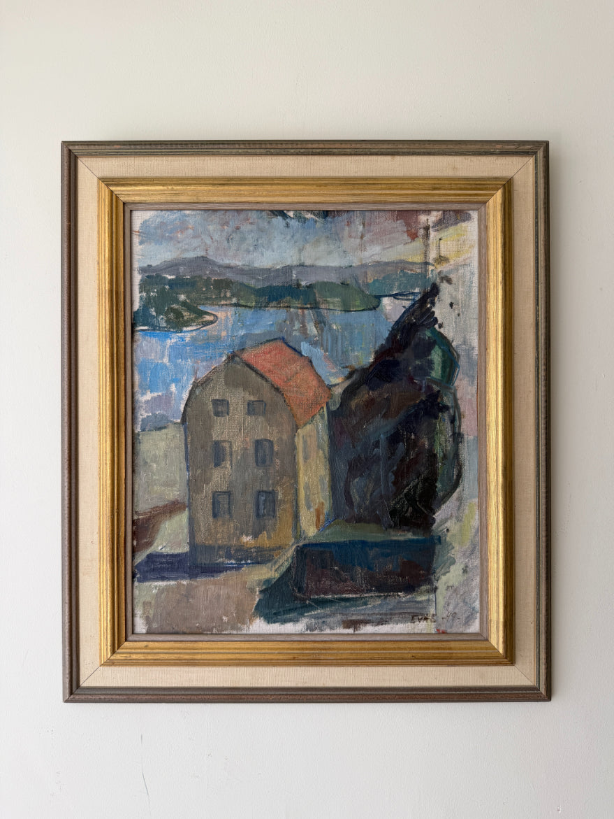 A framed vintage oil painting of a coastal landscape with a house, water, and dark trees. The artwork features a beige house with a red roof, blue water, and dark green/black foliage, enclosed in a gold and brown frame. Available at Hue.