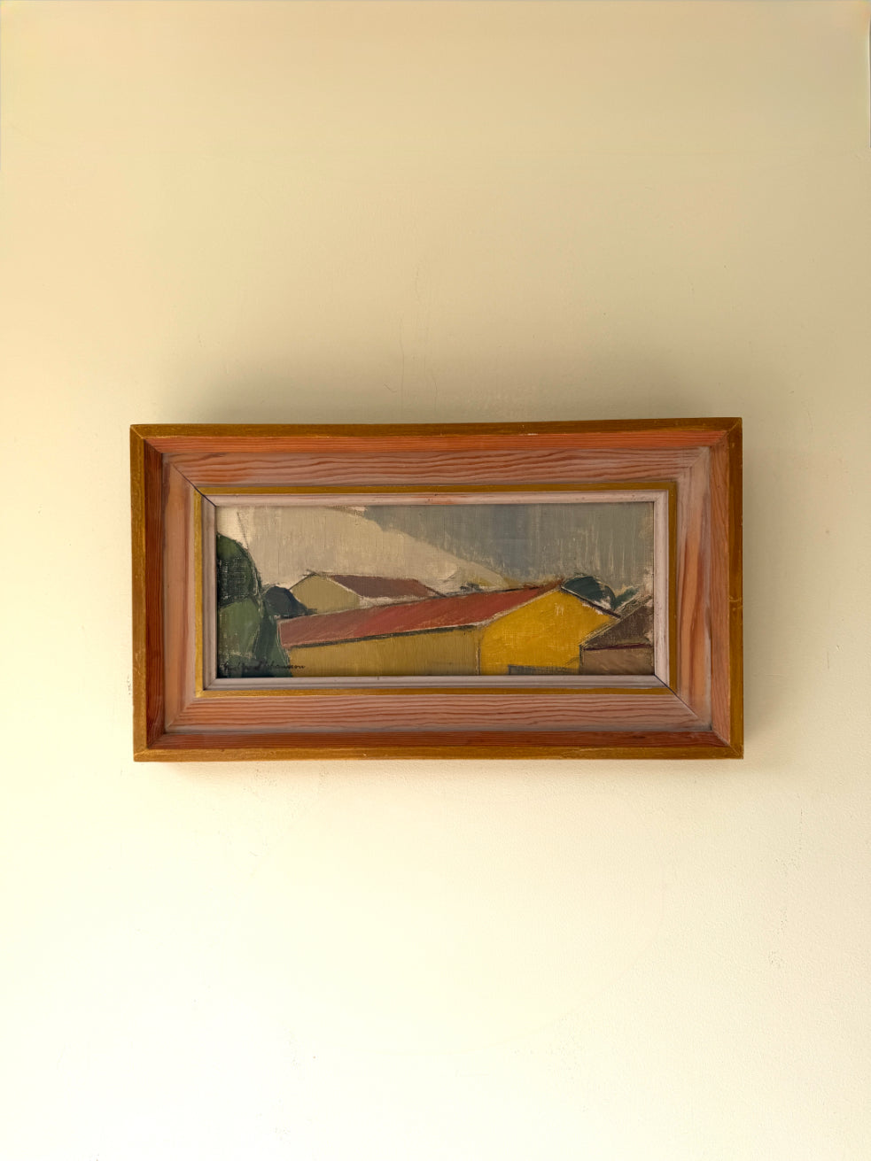 A framed vintage landscape oil painting of houses with red roofs and a yellow building. Available at Hue. 