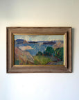 A framed vintage  landscape oil painting featuring blue water, green trees, and brown hills under a pale sky, housed in a rustic brown wooden frame with gold inner trim. Available at Hue. 