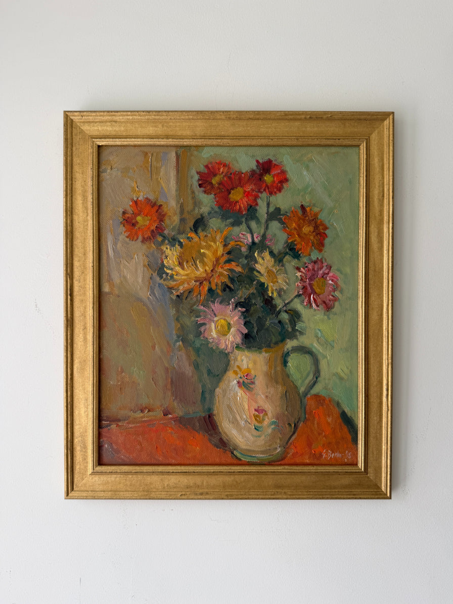A framed vintage oil painting of a floral bouquet in a ceramic pitcher. The painting features a variety of colorful flowers including red, orange, yellow, and pink, set against a muted green background. Available at Hue.