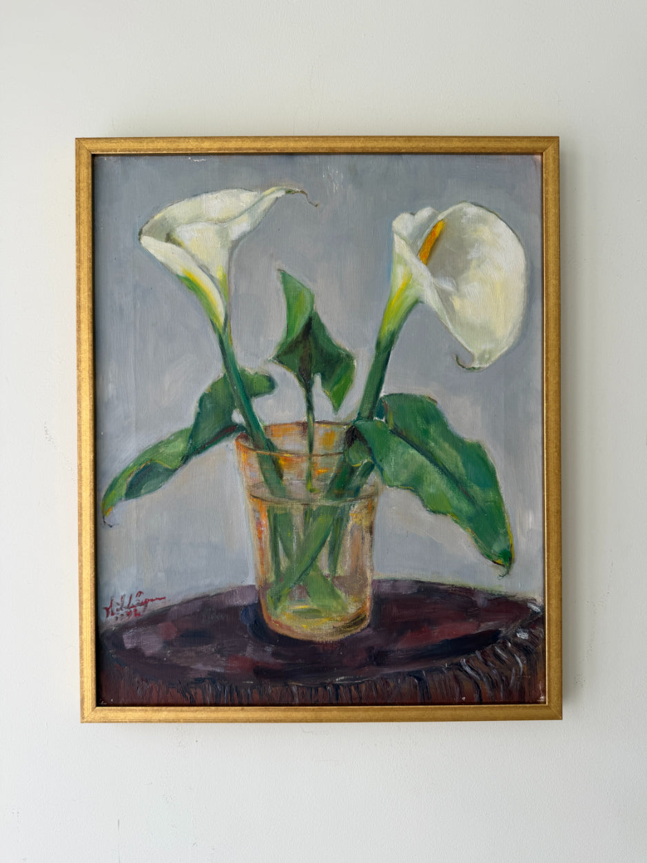 A framed vintage oil painting of white calla lilies in a clear glass vase on a dark surface, set against a muted gray background. Available at Hue. 