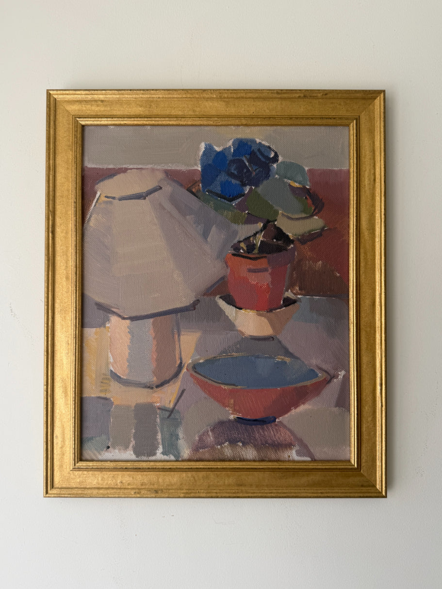 A framed vinatge still life oil painting featuring a lamp, flowers, and bowls, housed in a gold frame. Available at Hue. 