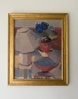 A framed vinatge still life oil painting featuring a lamp, flowers, and bowls, housed in a gold frame. Available at Hue. 