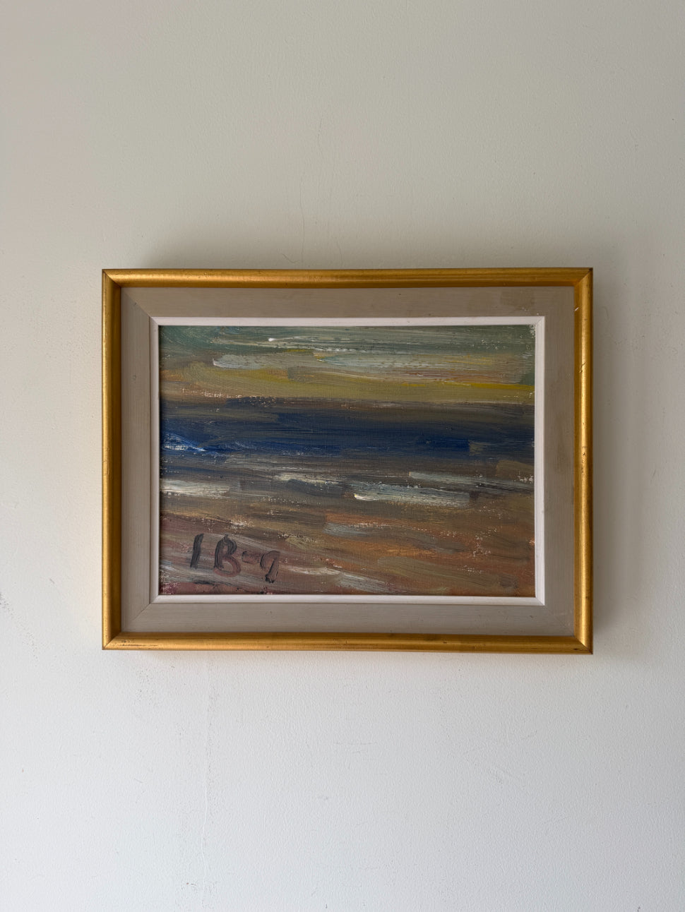 A framed vinatge landscape oil painting of a beach scene with blue water, sandy brown shore, and a gold frame. Available at Hue. 
