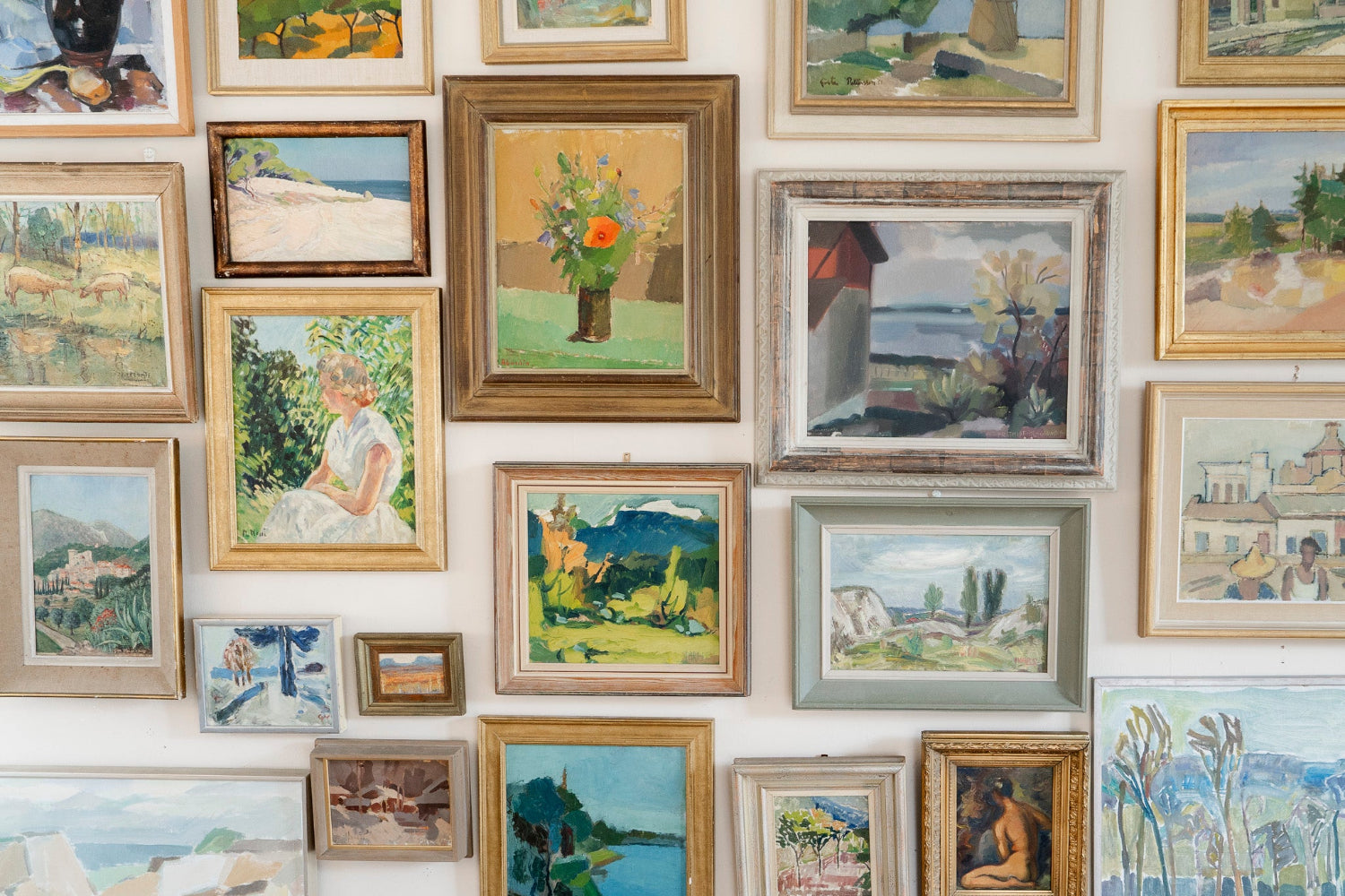 Eclectic gallery wall of original vintage oil paintings, landscapes and figurative artworks in gilt and painted frames, creating a layered collected interior by Hue + Holasz.