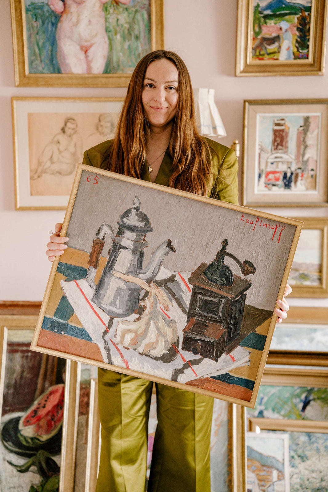 Woman holding an original vintage still life oil painting of a coffee pot and coffee grinder, surrounded by a colourful gallery wall of collected artwork by Hue + Holasz.