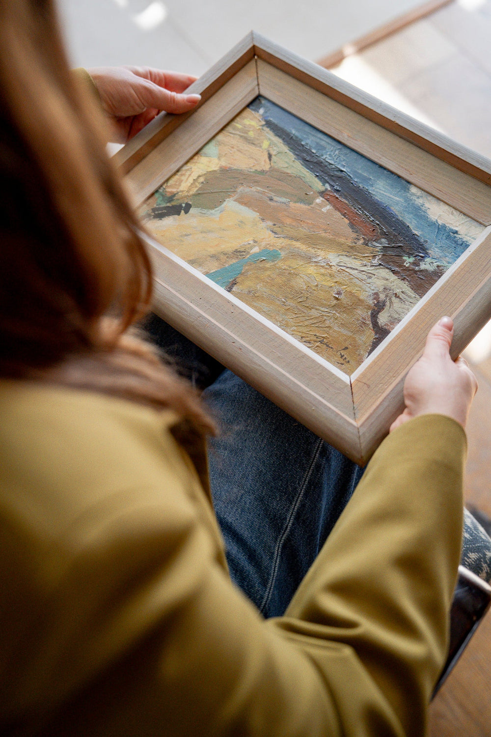 Art curator holding an original vintage landscape painting in a simple wooden frame, part of the curated Hue + Holasz art collection.